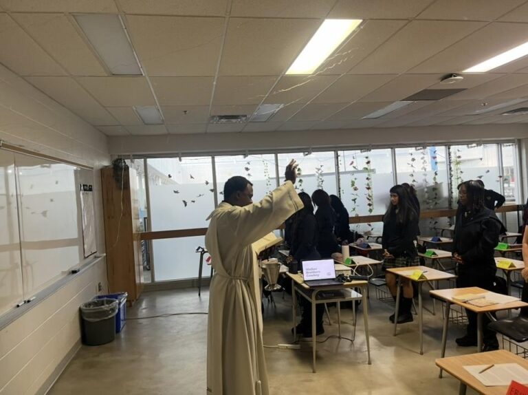 A priest blessing students in their classroom.